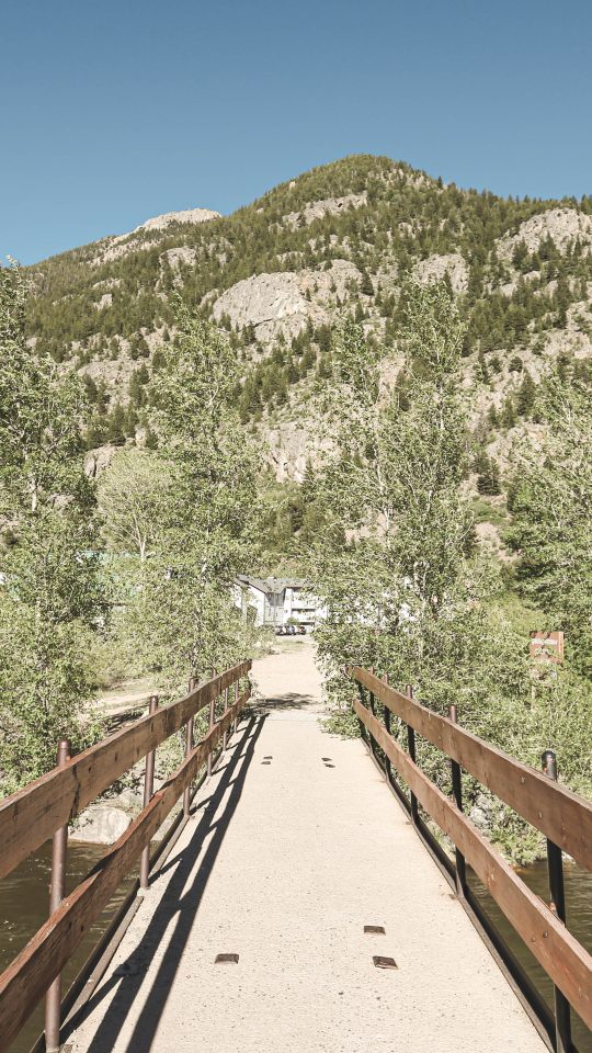 a wooden bridge over a river with mountains in the background at The Bighorn Crossing